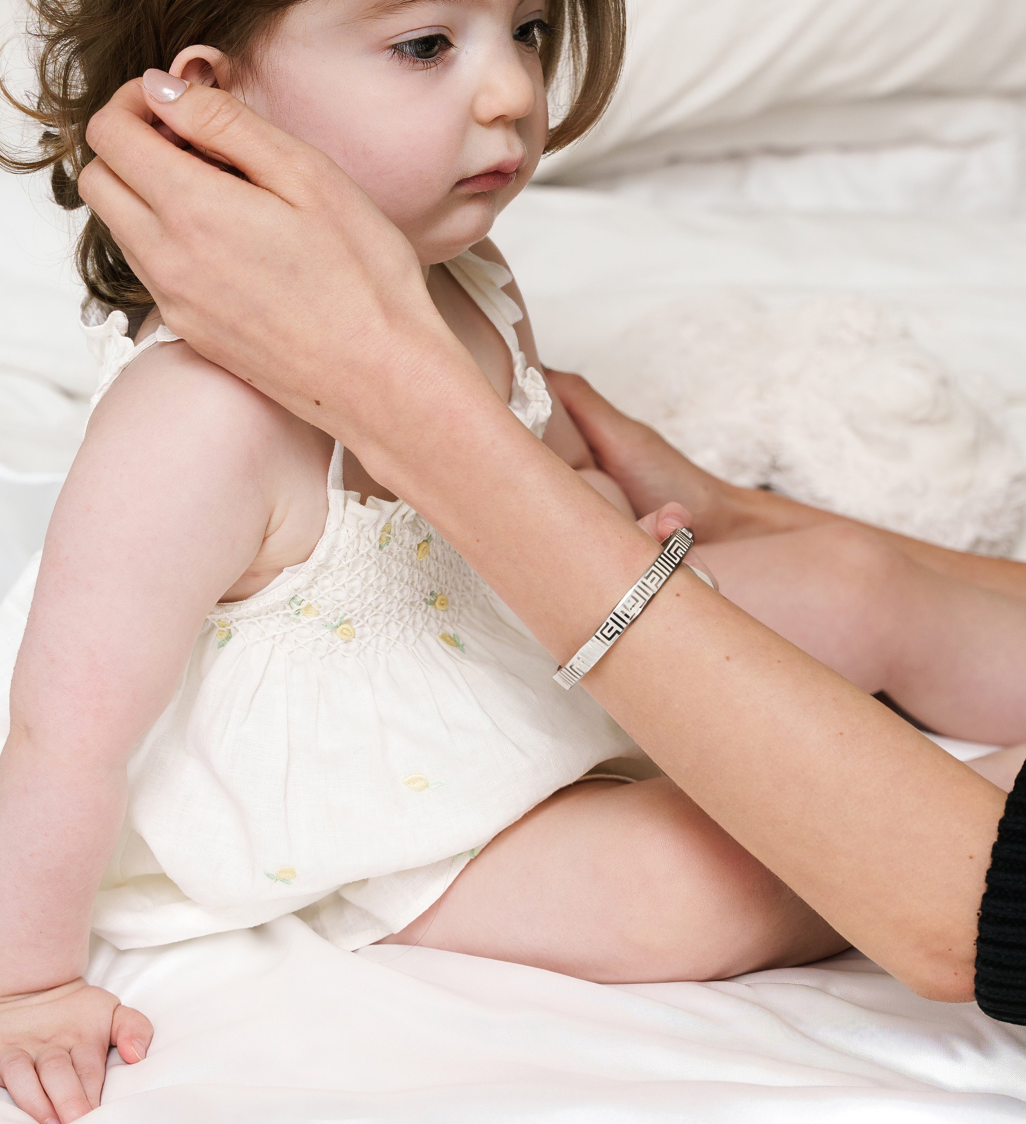 Baby being tenderly touched by mother in bed, wearing vivi coo motherhood jewellery.