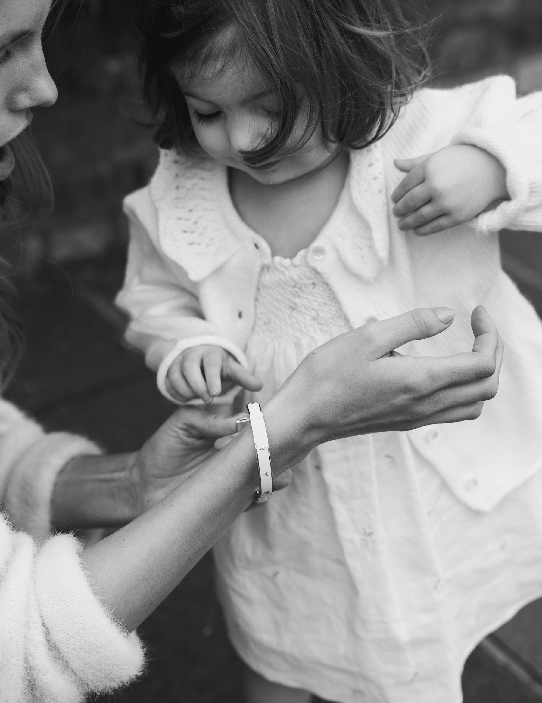 Black and white outdoor photo of a child admiring their mother’s Vivi Coo bracelet, symbolising their bond.