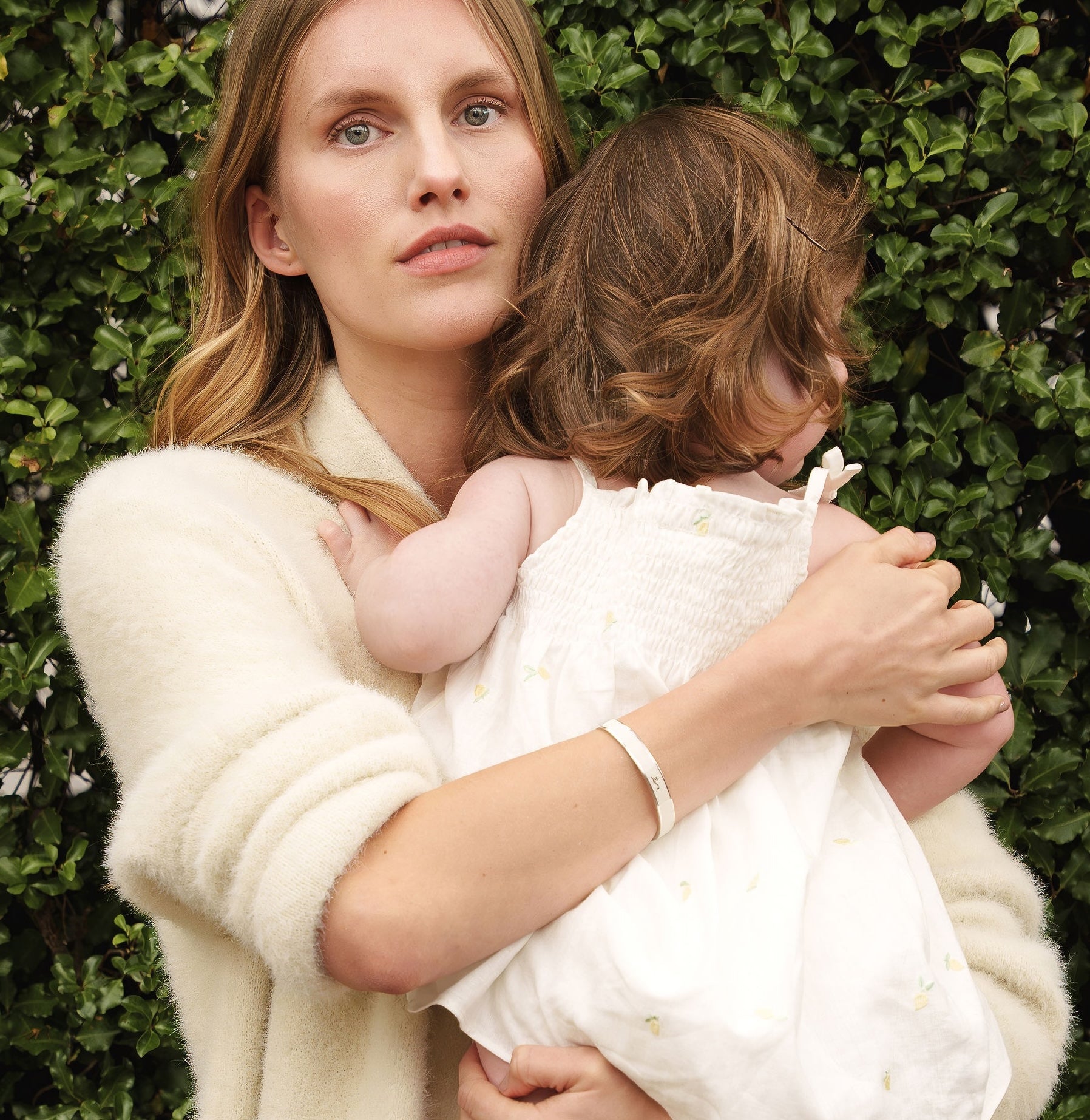 Mother holding child in garden whilst wearing her Vivi Coo Forever Coo bracelet. 
