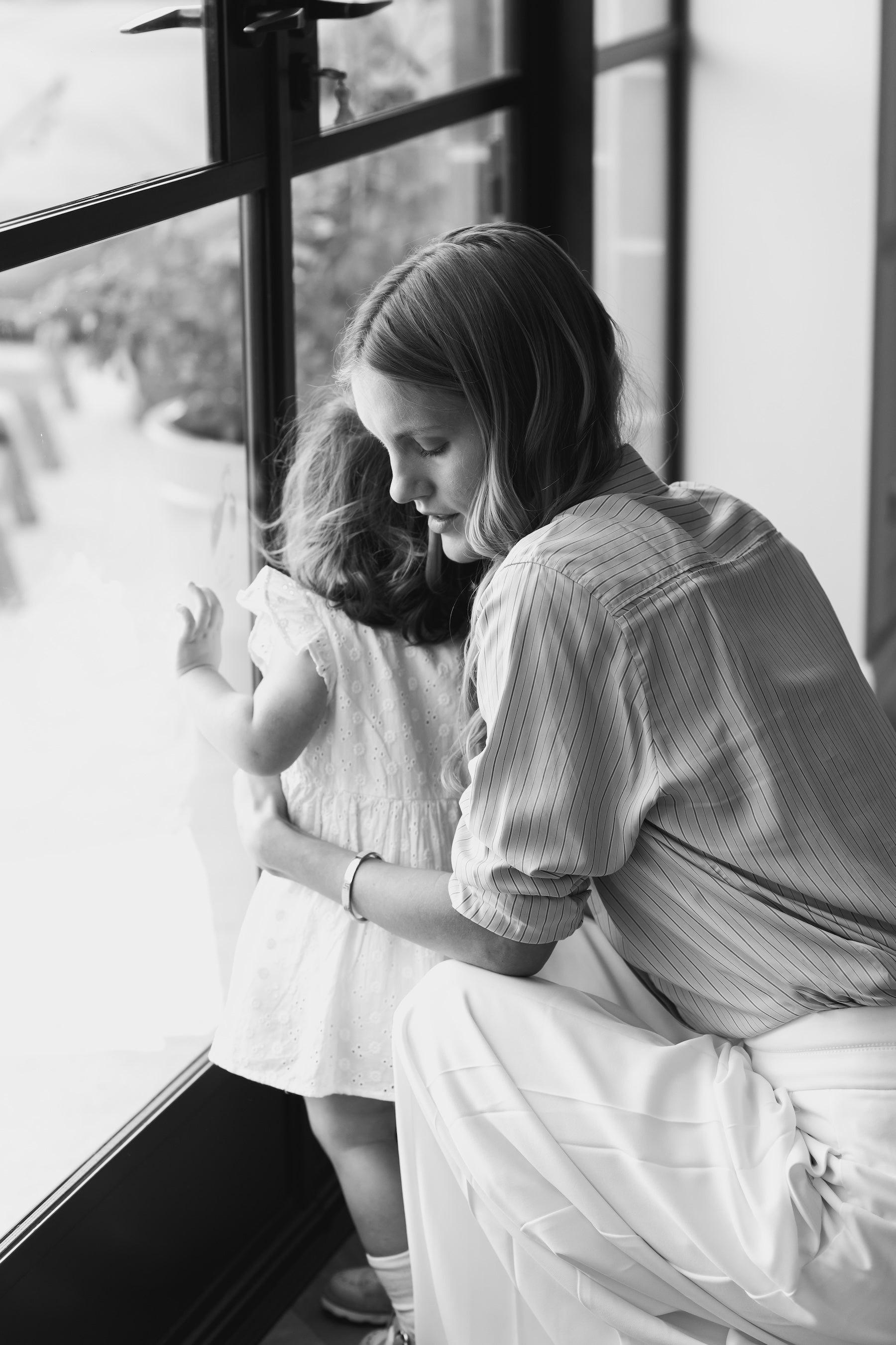 Mother wearing a Vivi Coo motherhood bracelet while holding her child and looking out of a window.