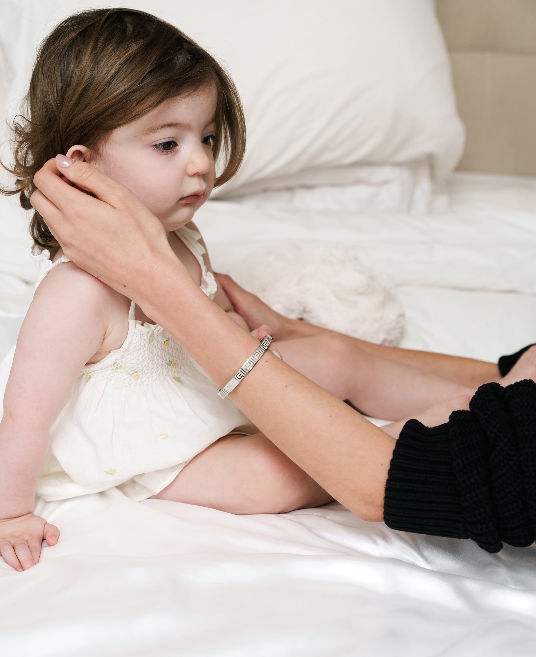 Baby being tenderly touched by mother in bed, wearing vivi coo motherhood jewellery.
